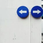Two blue signs pointing in opposite directions on a white wall