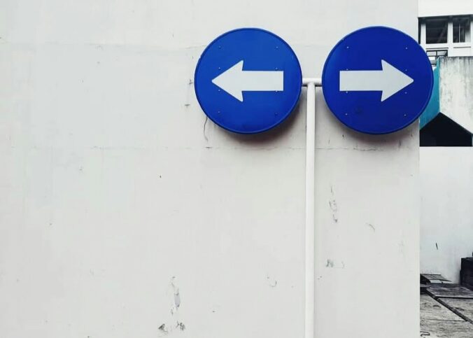 Two blue signs pointing in opposite directions on a white wall