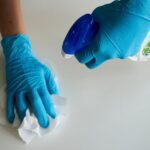 Close-up of hands wearing gloves cleaning a surface with disinfectant spray.
